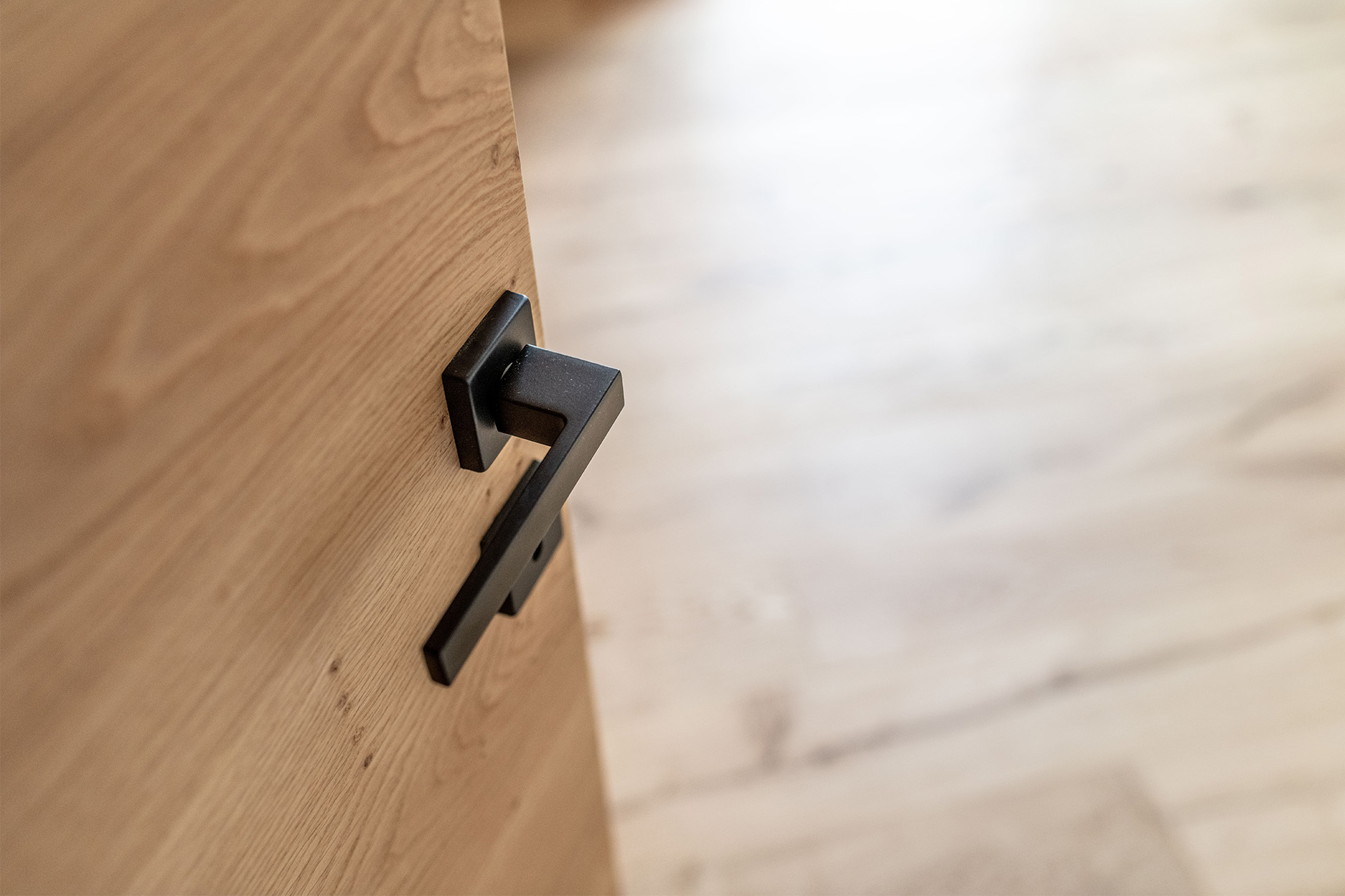 Schwarzer Türdrücker – Moderne Akzente an einer Holztür Nahaufnahme eines modernen, schwarzen Türdrückers an einer Holztür